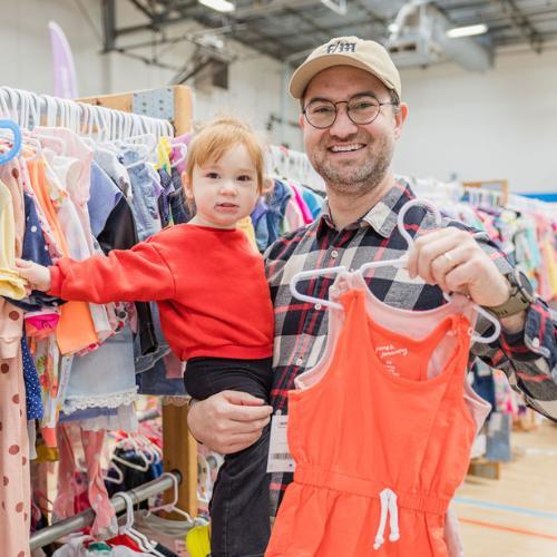 Three generations shop together at their local JBF sale. Mom carries baby in a baby carrier while grandmom stands behind them.